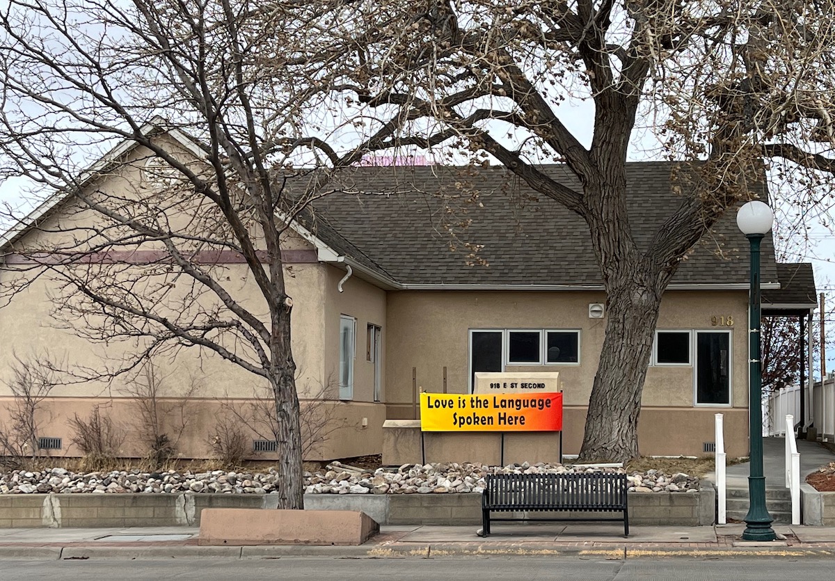 A tan building with a sign out front that says "love is the language spoken here"